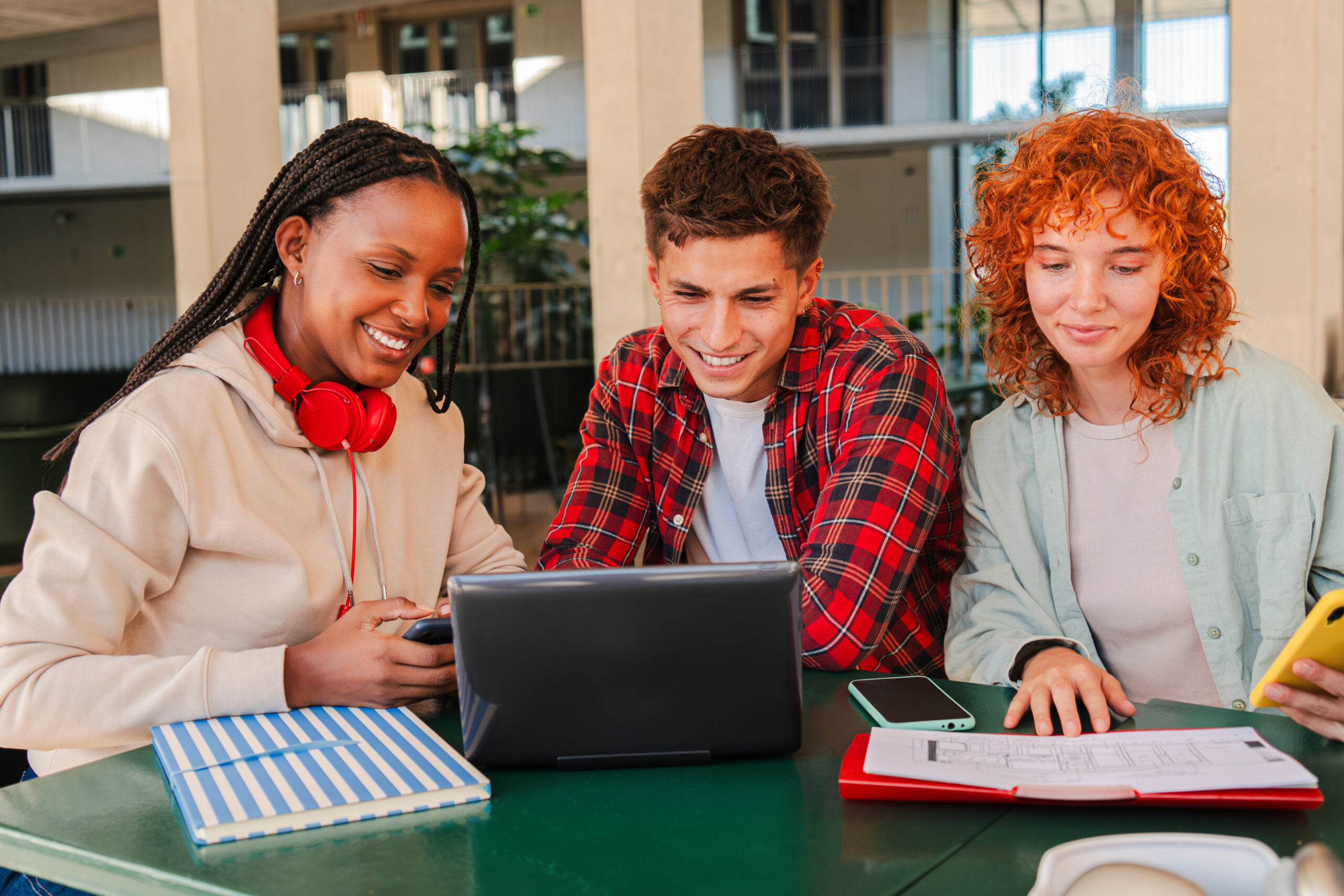 A dynamic trio of motivated students working together on a laptop, sharing knowledge and insights, while enjoying each other's company and fostering a spirit of teamwork in an academic environment filled with excitement